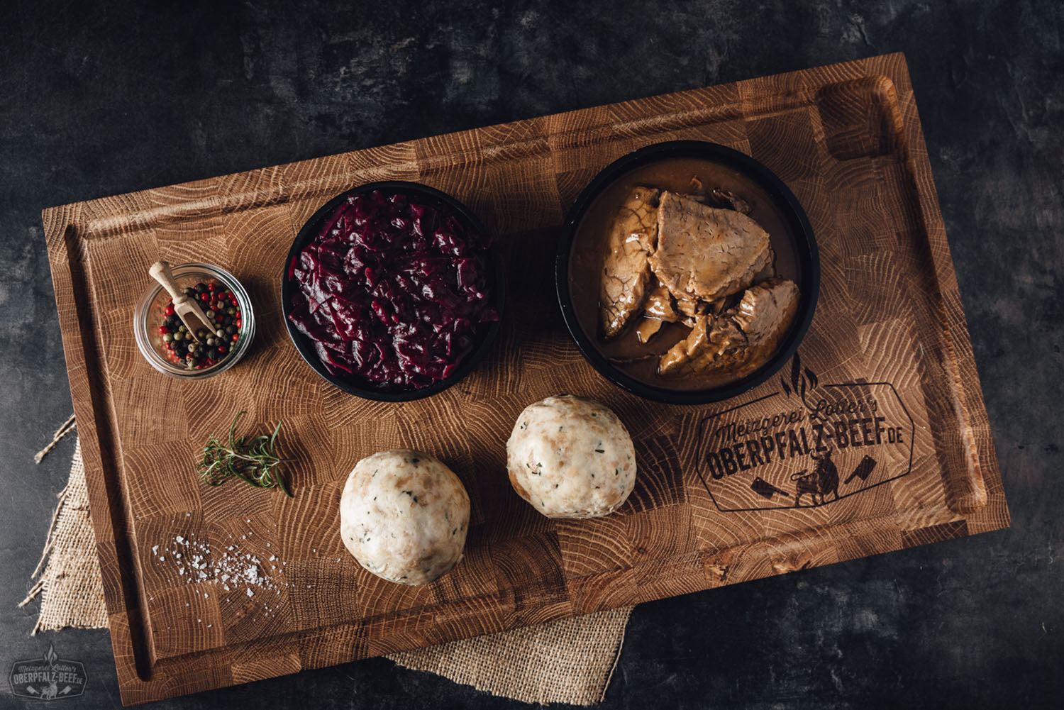 Ein hochwertiges, appetitlich angerichtetes Stück Oberpfälzer Rinderbraten in einer dekorativen Box, präsentiert auf einer rustikalen Unterlage mit frischen Kräutern und Beilagen, ideal für Gourmets und Feinschmecker.