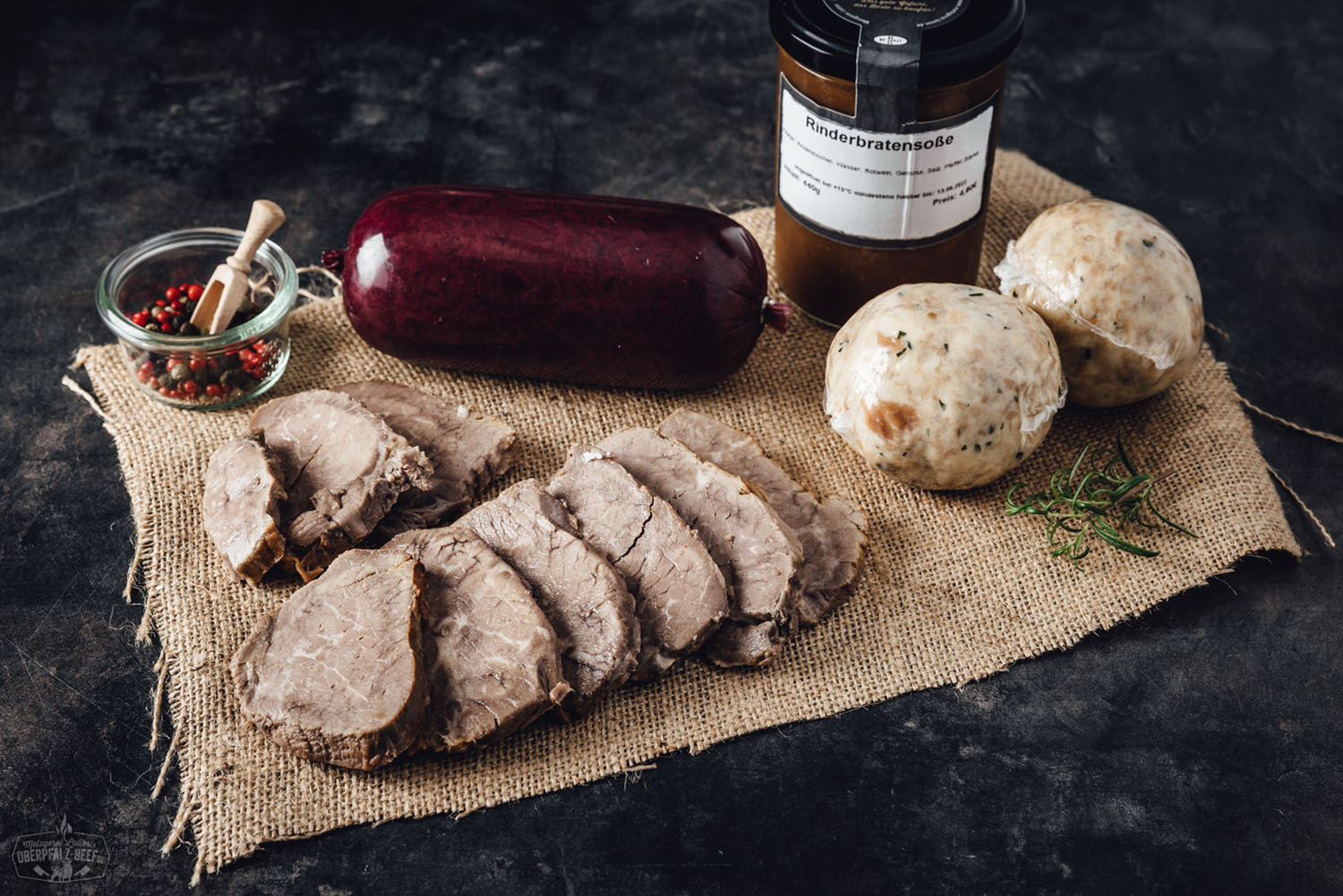 Ein hochwertiges, appetitlich angerichtetes Stück Oberpfälzer Rinderbraten in einer dekorativen Box, präsentiert auf einer rustikalen Unterlage mit frischen Kräutern und Beilagen, ideal für Gourmets und Feinschmecker.