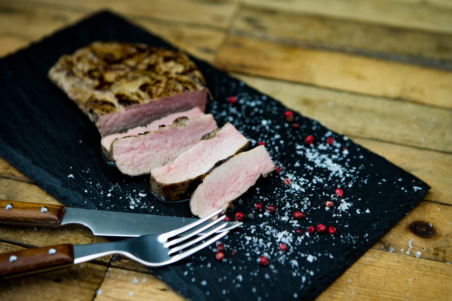 Pluma vom Oberpfälzer Landschwein auf Holzbrett serviert mit frischen Kräutern und Rosmarinzweigen.