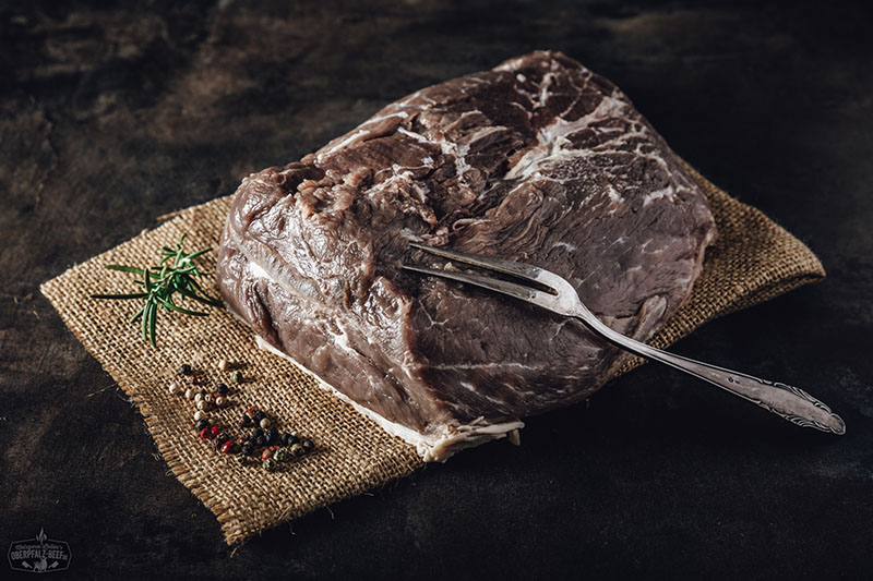 Eingelegter Sauerbraten aus Rindfleisch, umgeben von frischen Gewürzen und Kräutern, ideal für traditionelle deutsche Küche und Fleischliebhaber.