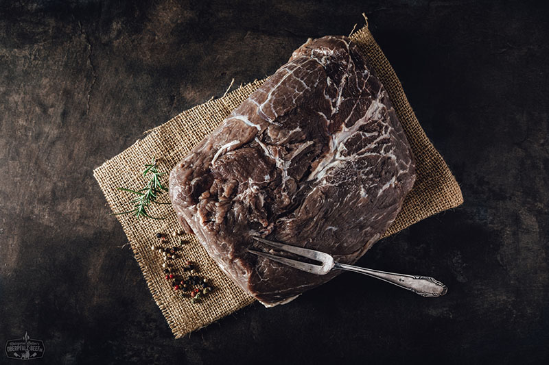 Eingelegter Sauerbraten aus Rindfleisch, umgeben von frischen Gewürzen und Kräutern, ideal für traditionelle deutsche Küche und Fleischliebhaber.