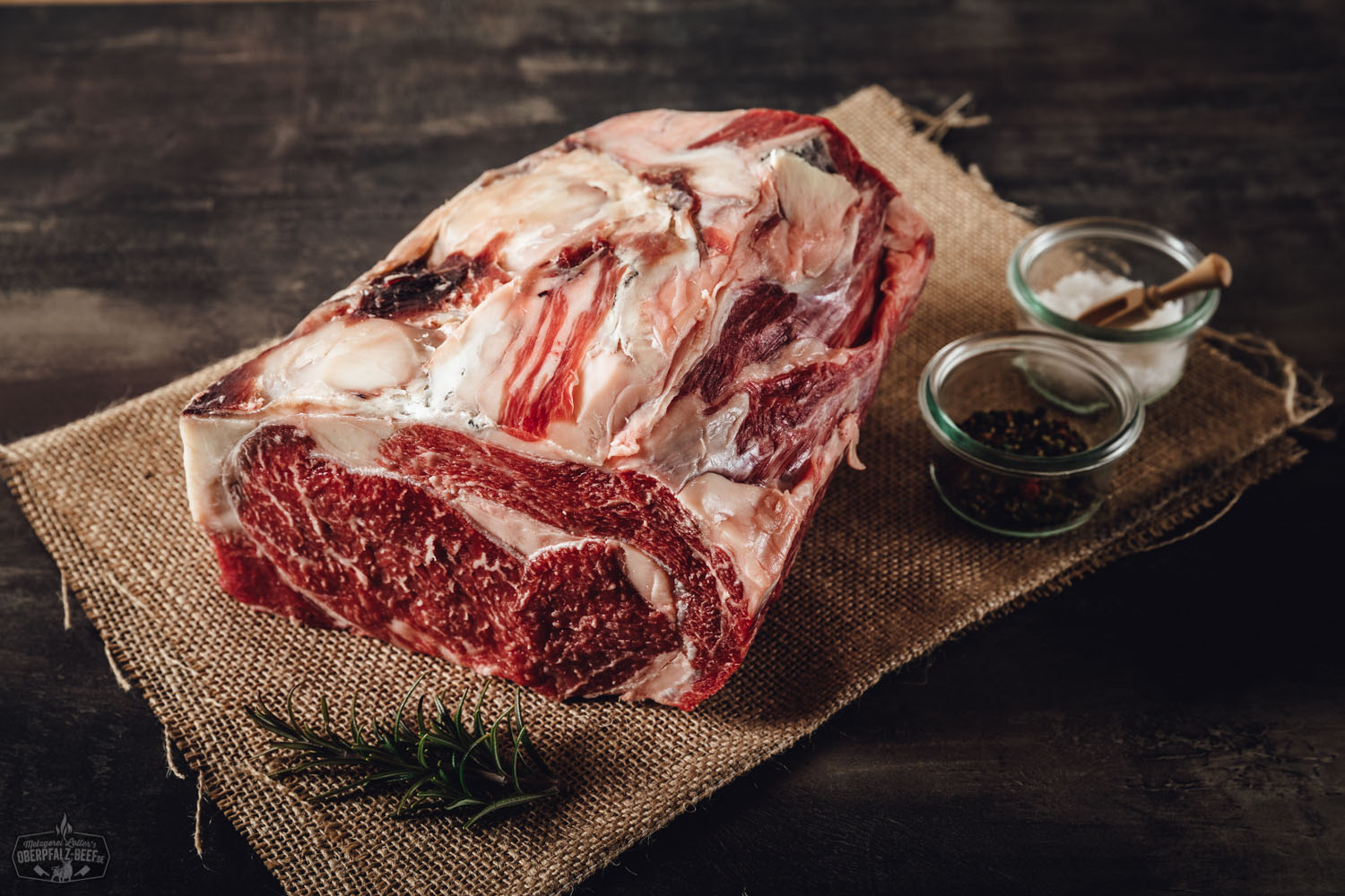 Ein saftiges Entrecôte-Rib-Eye-Steak von der alten Kuh, am Stück, dry-aged, mit tiefroter Fleischfarbe und feiner Marmorierung auf einem Holzbrett präsentiert.