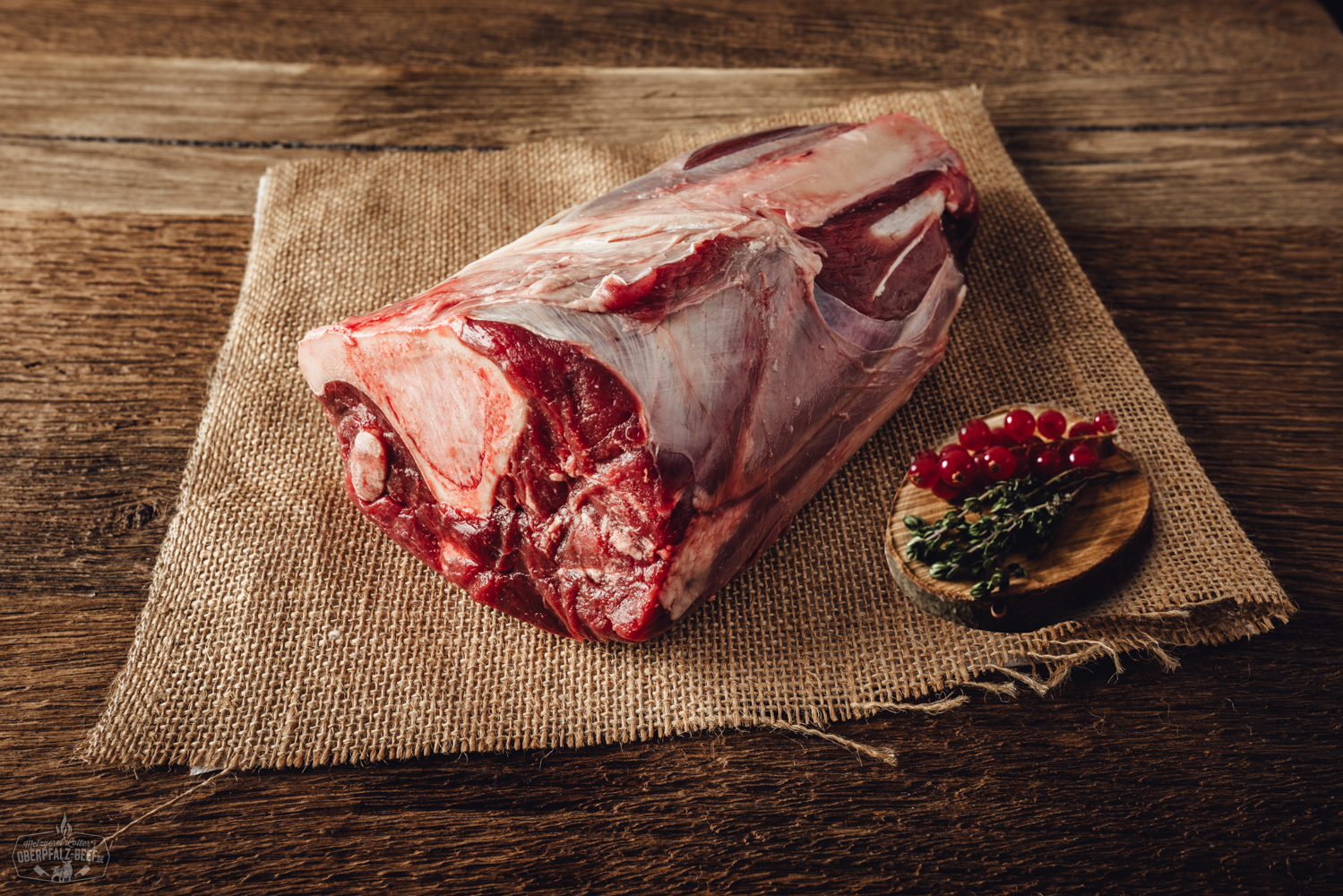 Haxe vom Oberpfälzer Hirsch, serviert auf einem Holzbrett mit frischen Kräutern garniert, traditionelles bayerisches Gericht aus hochwertigem Wildfleisch.