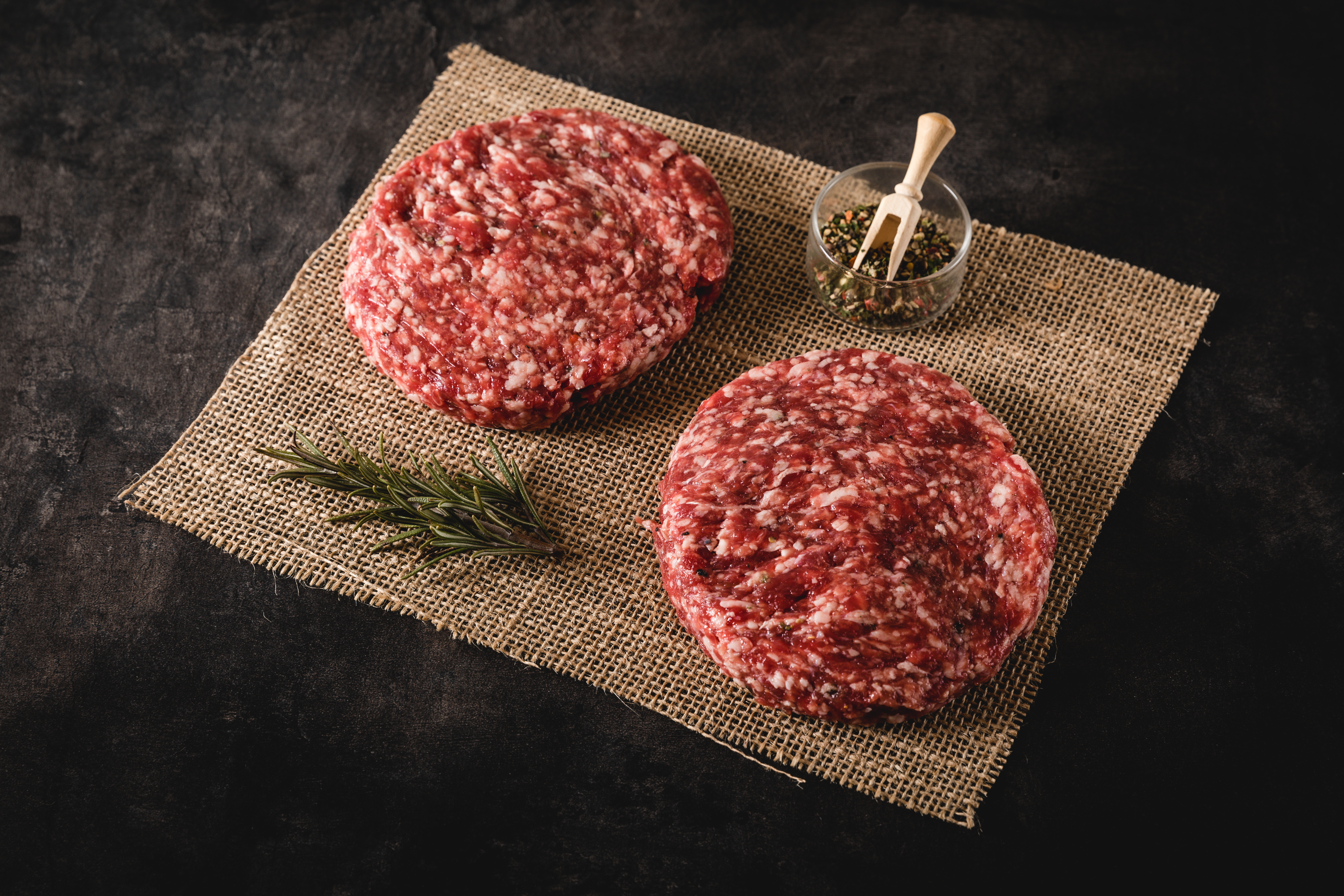 Wet-aged Beef Patties auf einem Schneidebrett mit Gewürzen und Kräutern – Premium Oberpfalz-Rindfleisch, perfekt für saftige Burger.